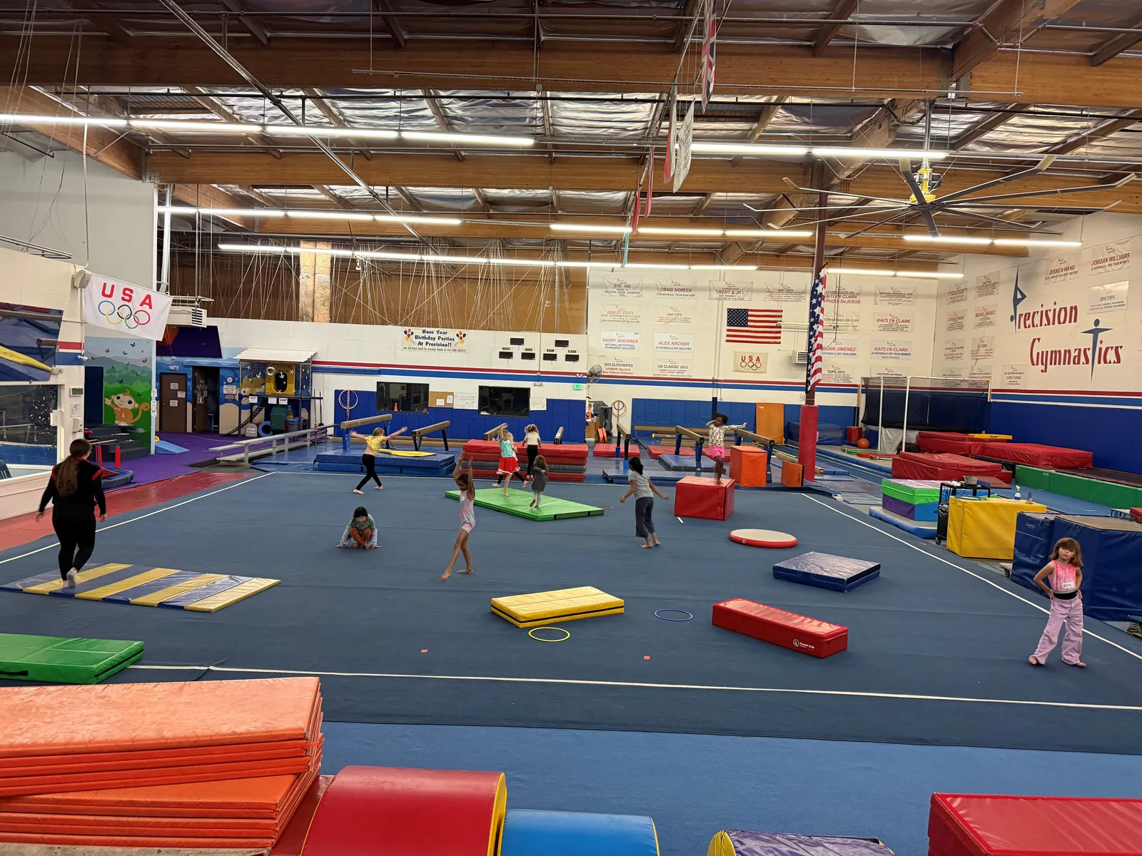 A wide view of the Precision gym floor, set up with mats, beams and equipment while children play