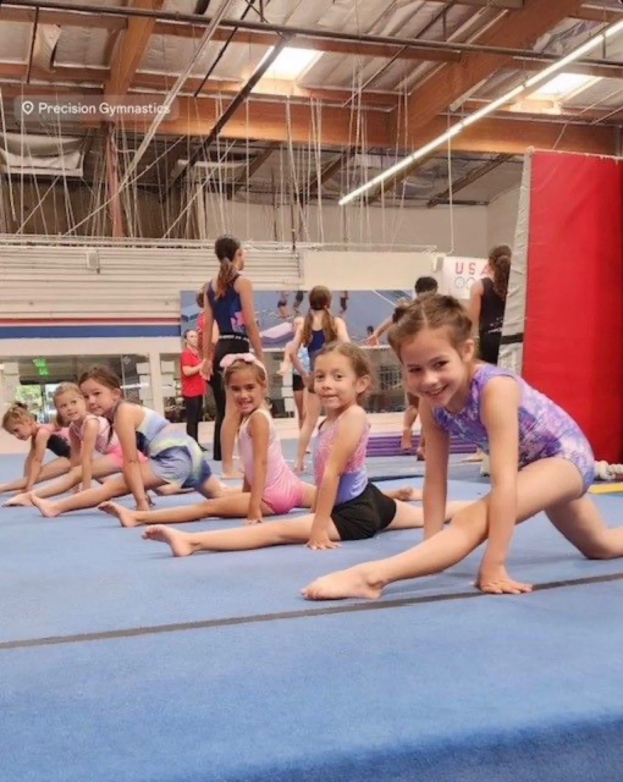 Preschool gymnasts stretching in straddle splits on the gym floor