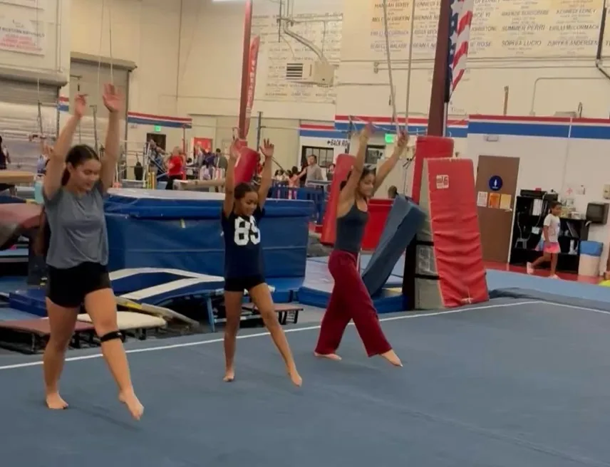 Three gymnasts finishing a pass on the tumbling floor